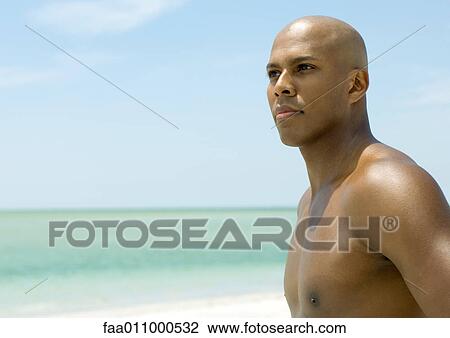 Stock Image - Young man on beach, looking away. Fotosearch