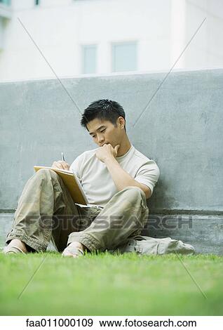 Young man sitting on grass, studying View Large Photo Image Stock Photo - Young man sitting on grass, studying. Fotosearch