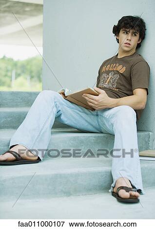 Young man sitting on steps with book View Large Photo Image Stock Photo - Young man sitting on steps with book. Fotosearch
