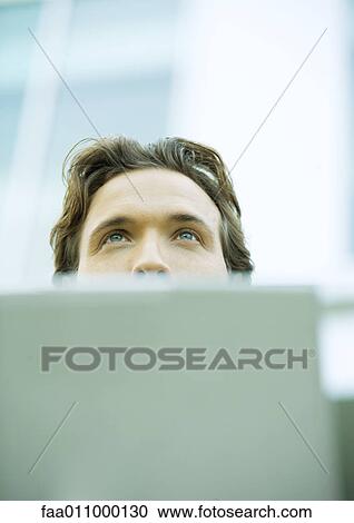 Young man with laptop, looking up View Large Photo Image Stock Image - Young man with laptop, looking up. Fotosearch