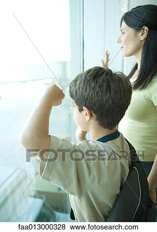 Boy and mother looking through window at airport View Large Photo Image Stock Photo - Boy and mother looking through window at airport. Fotosearch