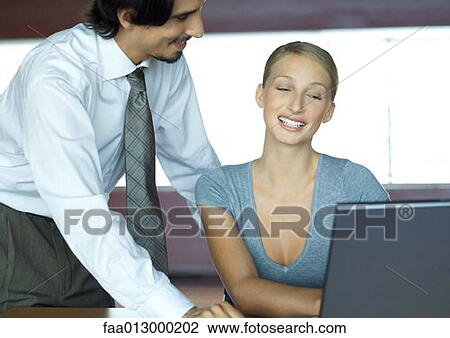 Stock Image - Businessman helping businesswoman with laptop. Fotosearch