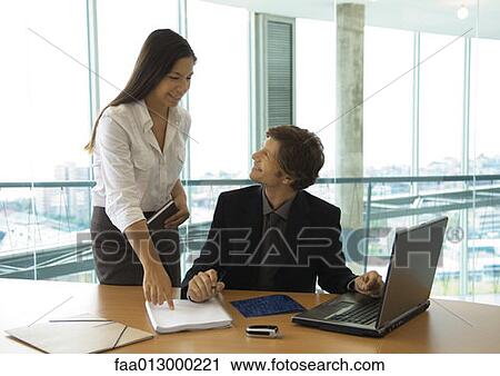Businessman working with laptop, speaking to female colleague View Large Photo Image Stock Image - Businessman working with laptop, speaking to female colleague. Fotosearch