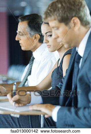 Businesspeople sitting, taking notes, woman glancing at man's paper View Large Photo Image Stock Image - Businesspeople sitting, taking notes, woman glancing at man's paper. Fotosearch