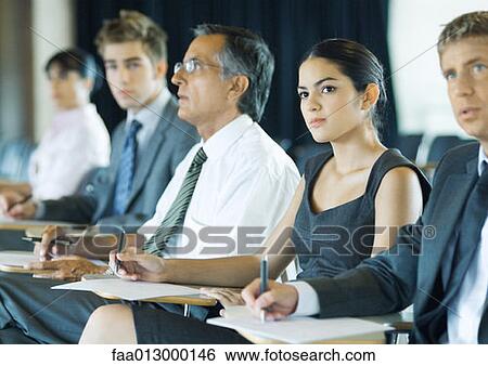 Businesspeople sitting, taking notes, looking attentively out of frame View Large Photo Image Stock Photograph - Businesspeople sitting, taking notes, looking attentively out of frame. Fotosearch