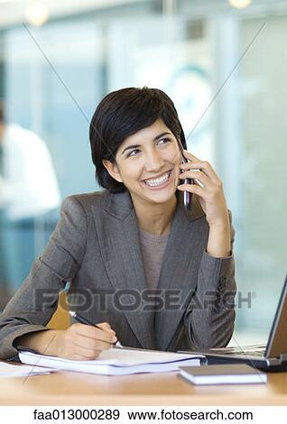 Businesswoman sitting at desk, using cell phone View Large Photo Image Stock Photo - Businesswoman sitting at desk, using cell phone. Fotosearch