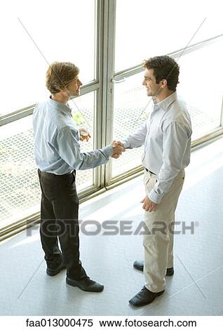 Executives shaking hands, one holding glass of champagne View Large Photo Image Stock Photography - Executives shaking hands, one holding glass of champagne. Fotosearch