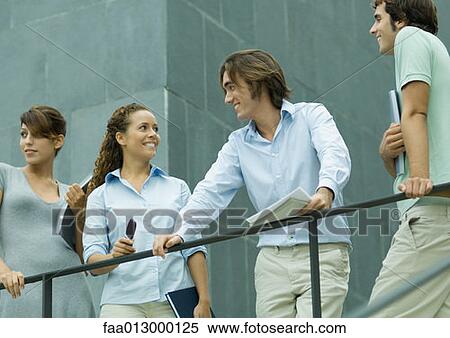 Stock Photography - Four young executives standing next to railing, one man and woman smiling at each other. Fotosearch