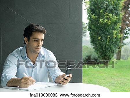 Man sitting at table outdoors, looking at cell phone and writing View Large Photo Image Stock Image - Man sitting at table outdoors, looking at cell phone and writing. Fotosearch