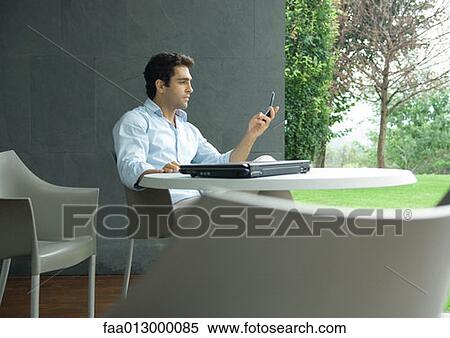 Man sitting at table outdoors, looking at cell phone View Large Photo Image Stock Photography - Man sitting at table outdoors, looking at cell phone. Fotosearch