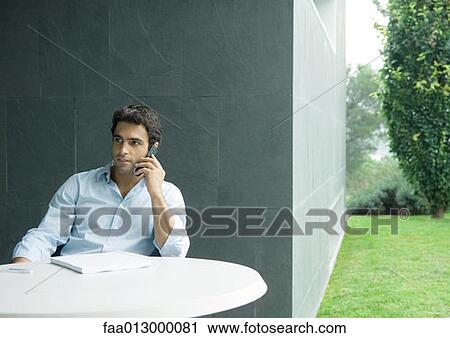Man sitting at table outdoors, using cell phone View Large Photo Image Stock Image - Man sitting at table outdoors, using cell phone. Fotosearch