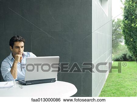 Man sitting at table outdoors, using laptop View Large Photo Image Stock Photograph - Man sitting at table outdoors, using laptop. Fotosearch