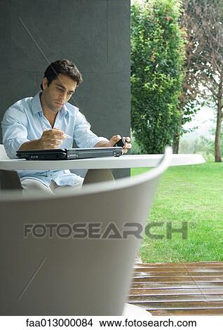 Man sitting at table outdoors, working View Large Photo Image Picture - Man sitting at table outdoors, working. Fotosearch