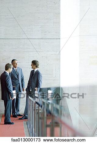Three businessman standing, talking at end of corridor View Large Photo Image Stock Image - Three businessman standing, talking at end of corridor. Fotosearch