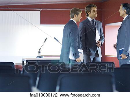 Stock Image - Three businessman standing, talking in conference room. Fotosearch