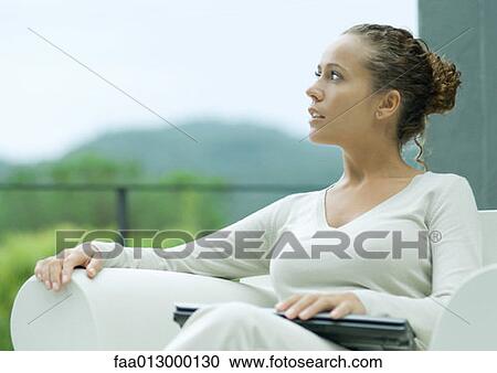 Stock Image - Woman sitting outdoors in armchair, with laptop closed on lap. Fotosearch