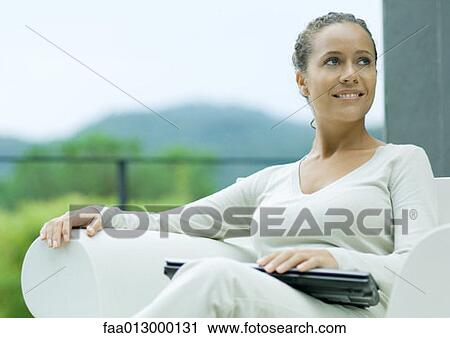 Woman sitting outdoors in armchair, with laptop closed on lap, smiling View Large Photo Image Stock Image - Woman sitting outdoors in armchair, with laptop closed on lap, smiling. Fotosearch