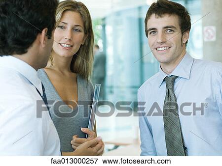 Stock Photo - Young executives talking, man looking at camera. Fotosearch