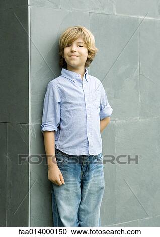 Stock Image - Boy leaning against wall, smiling, portrait. Fotosearch