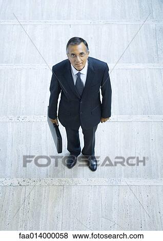 Businessman standing holding briefcase, portrait, high angle view View Large Photo Image Stock Photo - Businessman standing holding briefcase, portrait, high angle view. Fotosearch