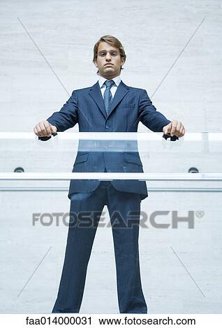 Businessman standing with hands resting on transparent guard rail, portrait, low angle view View Large Photo Image Stock Image - Businessman standing with hands resting on transparent guard rail, portrait, low angle view. Fotosearch