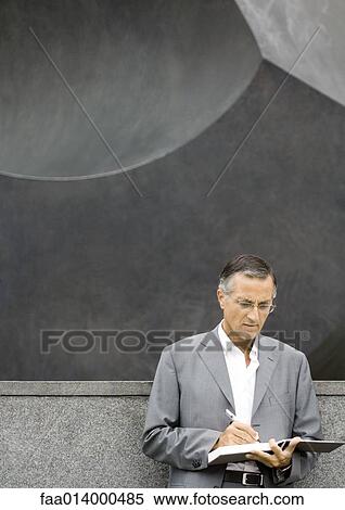 Businessman standing, writing in agenda View Large Photo Image Stock Photography - Businessman standing, writing in agenda. Fotosearch