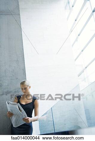 Picture - Businesswoman leaning against glass guard rail, reading newspaper. Fotosearch