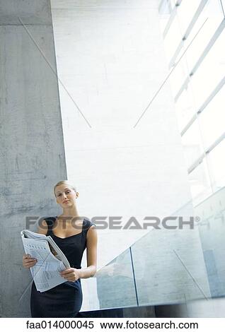 Stock Photography - Businesswoman leaning against glass guard rail, reading newspaper. Fotosearch