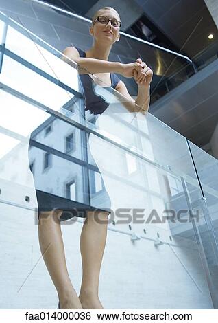 Stock Photograph - Businesswoman leaning against guard rail, low angle view. Fotosearch