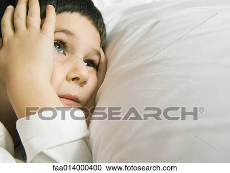 Child lying in bed holding head View Large Photo Image Stock Image - Child lying in bed holding head. Fotosearch