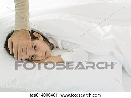 Child lying in bed with father's hand on forehead View Large Photo Image Stock Image - Child lying in bed with father's hand on forehead. Fotosearch