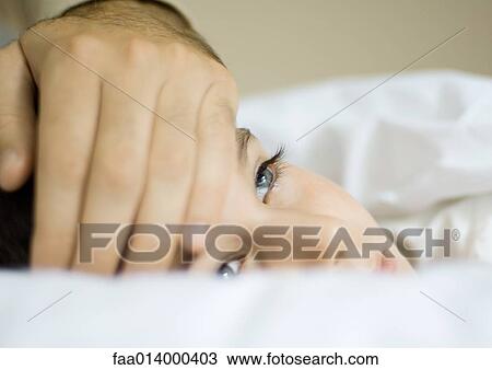 Stock Image - Child lying in bed with father's hand on forehead. Fotosearch