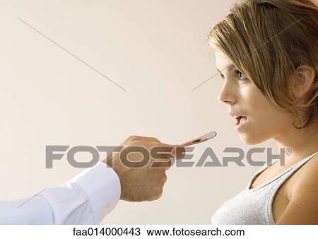 Doctor holding out tongue depressor toward young woman's mouth View Large Photo Image Stock Image - Doctor holding out tongue depressor toward young woman's mouth. Fotosearch