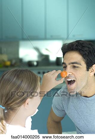 Girl holding up cherry tomato to man's nose View Large Photo Image Stock Photography - Girl holding up cherry tomato to man's nose. Fotosearch