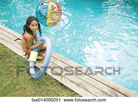 Stock Image - Girl sitting by edge of pool, holding floating ring. Fotosearch