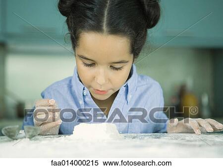 Stock Photography - Girl standing at kitchen counter, looking down at mound of dough. Fotosearch
