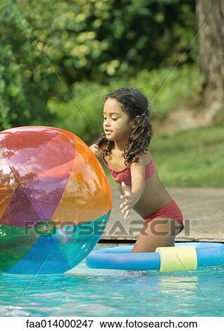 Stock Photo - Girl standing in pool, reaching for beach ball. Fotosearch
