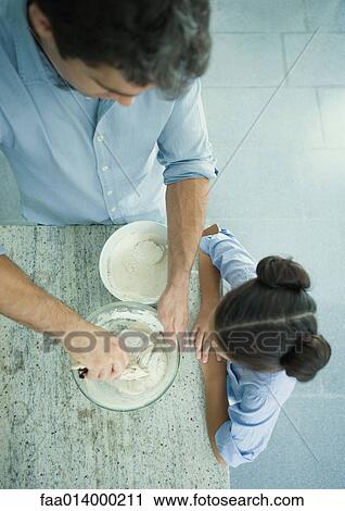 Stock Image - Girl watching as father mixes dough, high angle view. Fotosearch