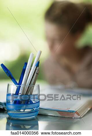 Glass full of pens, child doing homework in background View Large Photo Image Stock Photograph - Glass full of pens, child doing homework in background. Fotosearch
