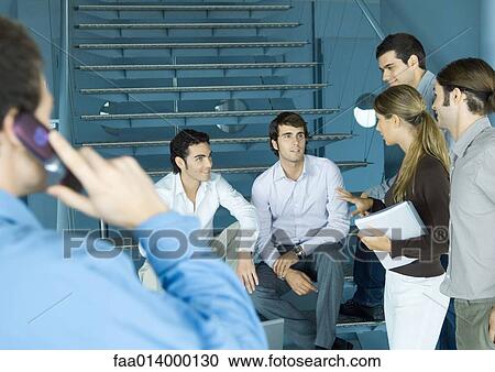 Stock Image - Group of colleagues gathered around stairs, talking. Fotosearch