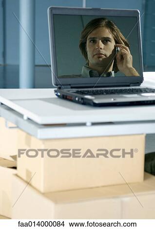 Picture - Image of man using cell phone reflected in laptop screen. Fotosearch