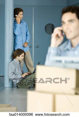 Male colleagues using laptop and cell phone, cardboard boxes in foreground View Large Photo Image Stock Photograph - Male colleagues using laptop and cell phone, cardboard boxes in foreground. Fotosearch