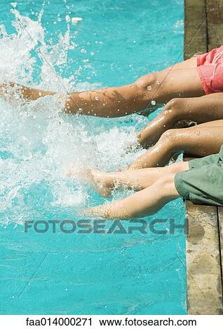 Stock Image - Man and children sitting on edge of swimming pool, splashing with legs. Fotosearch