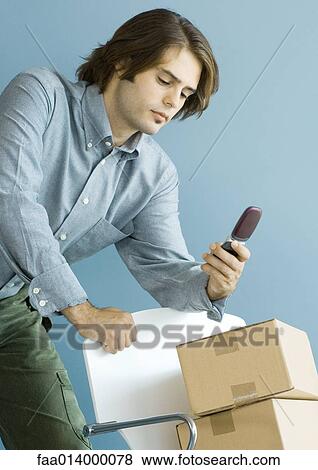 Man looking at cell phone, leaning on chair piled with cardboard boxes View Large Photo Image Stock Photo - Man looking at cell phone, leaning on chair piled with cardboard boxes. Fotosearch