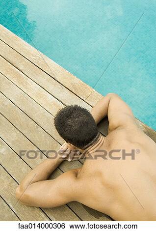 Stock Photograph - Man lying by edge of swimming pool, waist down. Fotosearch