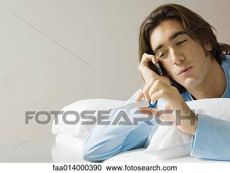 Man lying in bed, using cell phone and holding up thermometer View Large Photo Image Stock Image - Man lying in bed, using cell phone and holding up thermometer. Fotosearch