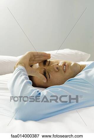 Man lying on bed with hand on forehead, making face View Large Photo Image Stock Photo - Man lying on bed with hand on forehead, making face. Fotosearch