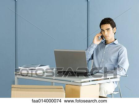 Man sitting at desk, using phone View Large Photo Image Picture - Man sitting at desk, using phone. Fotosearch
