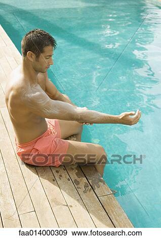 Man sitting by edge of swimming pool, applying sunscreen View Large Photo Image Stock Photo - Man sitting by edge of swimming pool, applying sunscreen. Fotosearch