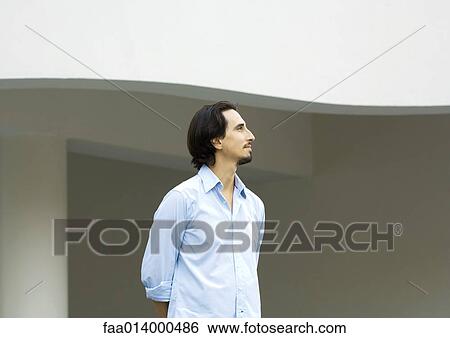 Man standing with arms behind back, looking out of frame View Large Photo Image Stock Photograph - Man standing with arms behind back, looking out of frame. Fotosearch